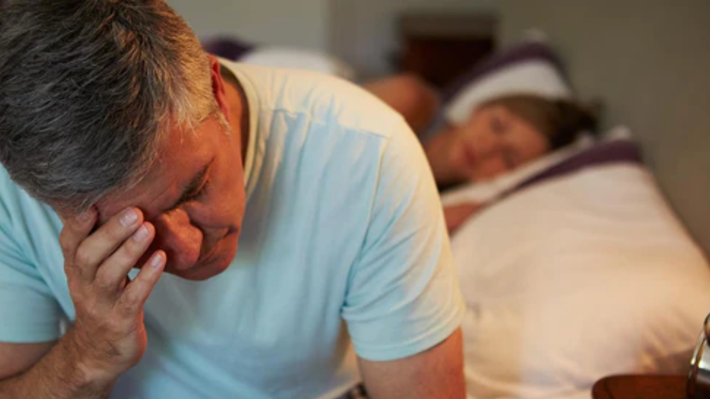 man awake in bed suffering with insomnia due to enlarged prostate