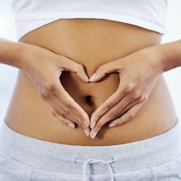 Close-up of a person's hands forming a heart shape over their stomach.