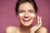 Smiling woman applying skin cream to her cheeks