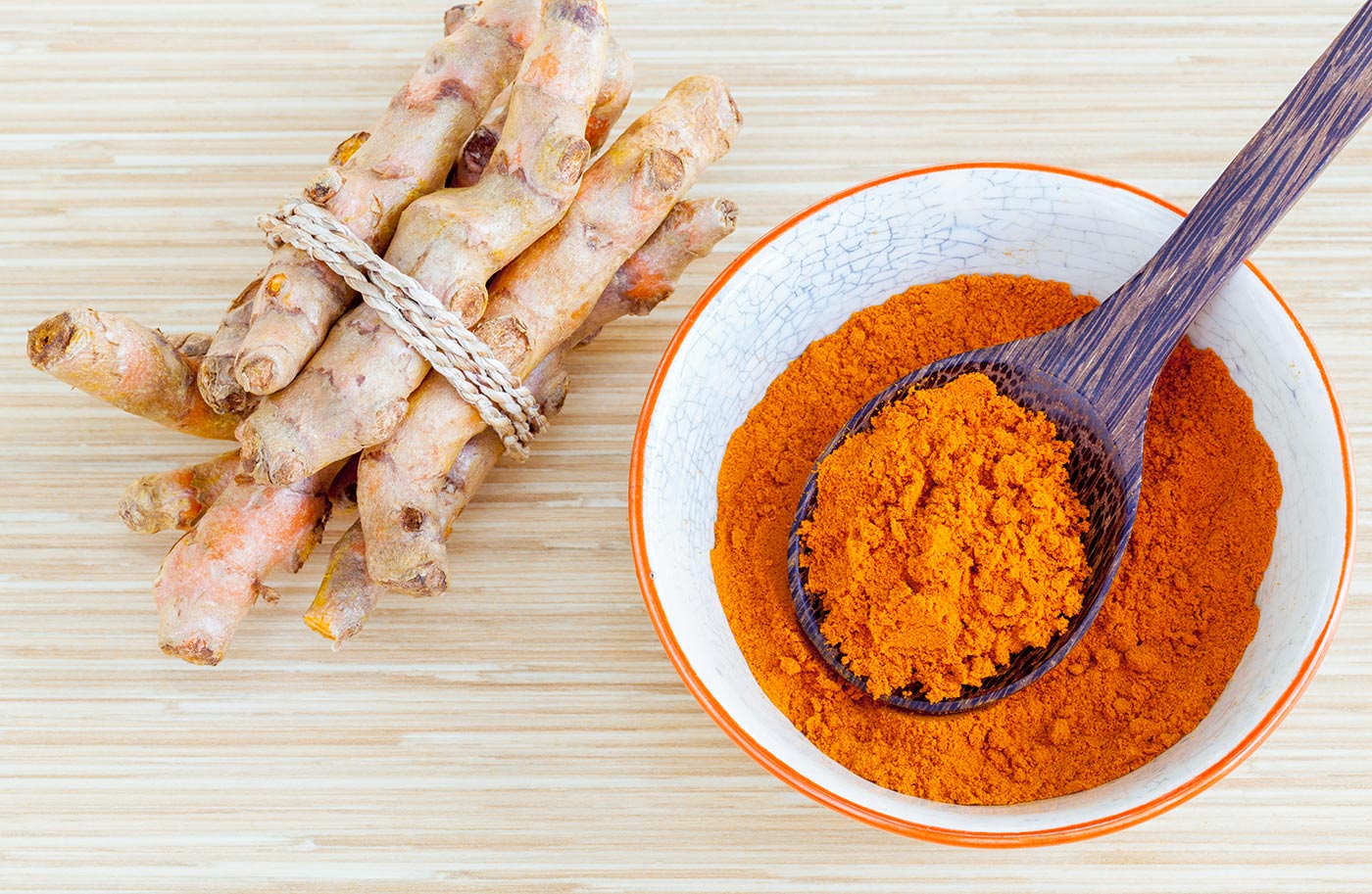 Turmeric roots tied together and and turmeric powder extract in a bowl