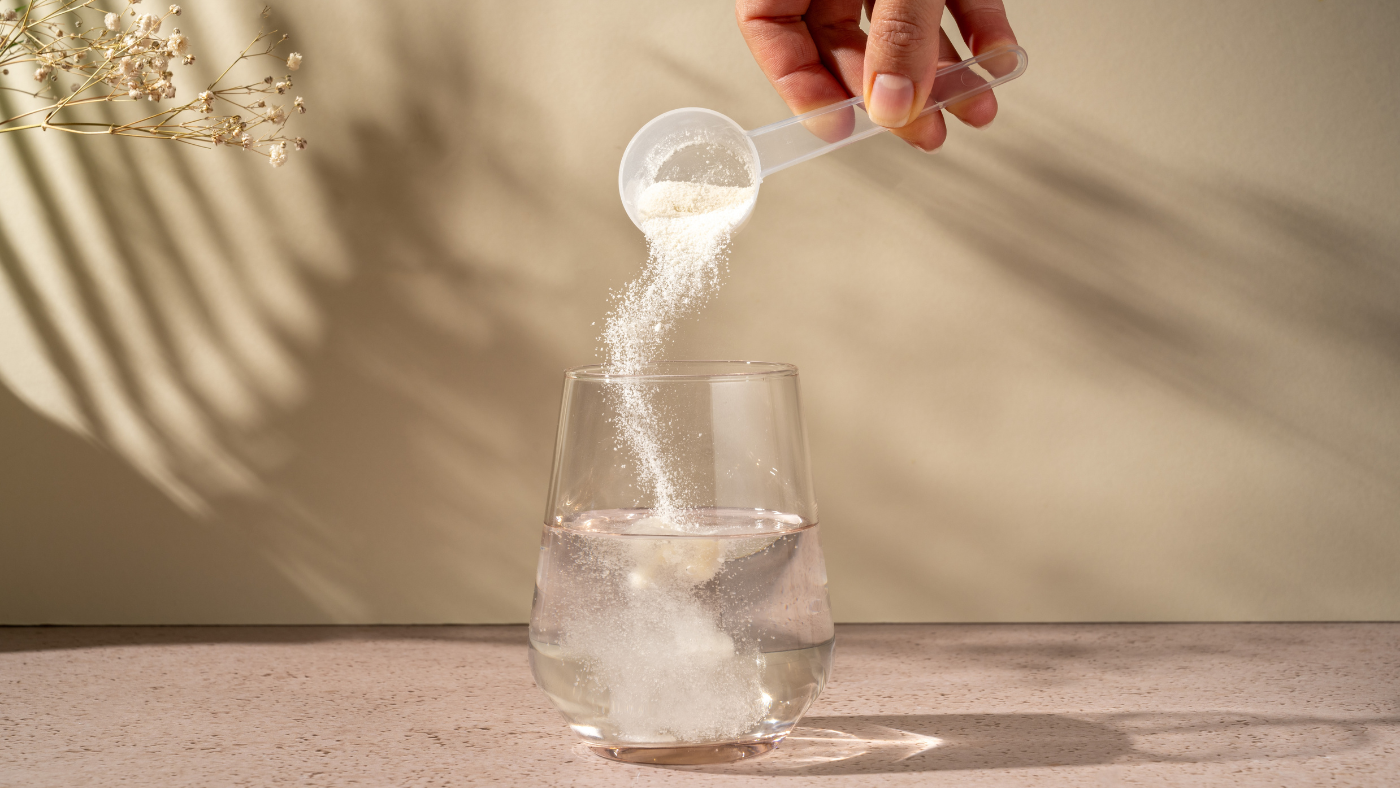 Glass of water with a scoop of collagen powder being added