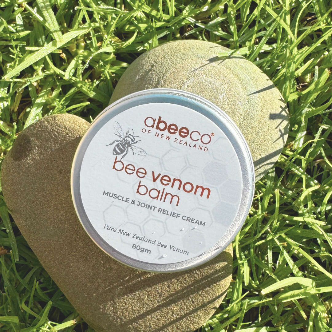 Abeeco bee venom balm container on a rock with grass in the background