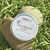 Abeeco bee venom balm container on a rock with grass in the background