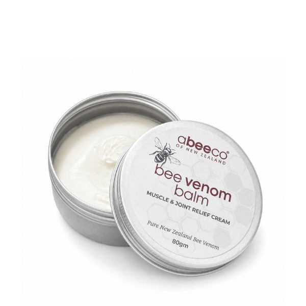 An open round silver metal tin of abeeco bee venom balm, showing the white cream inside, with the lid leaning against it on a clean white background.