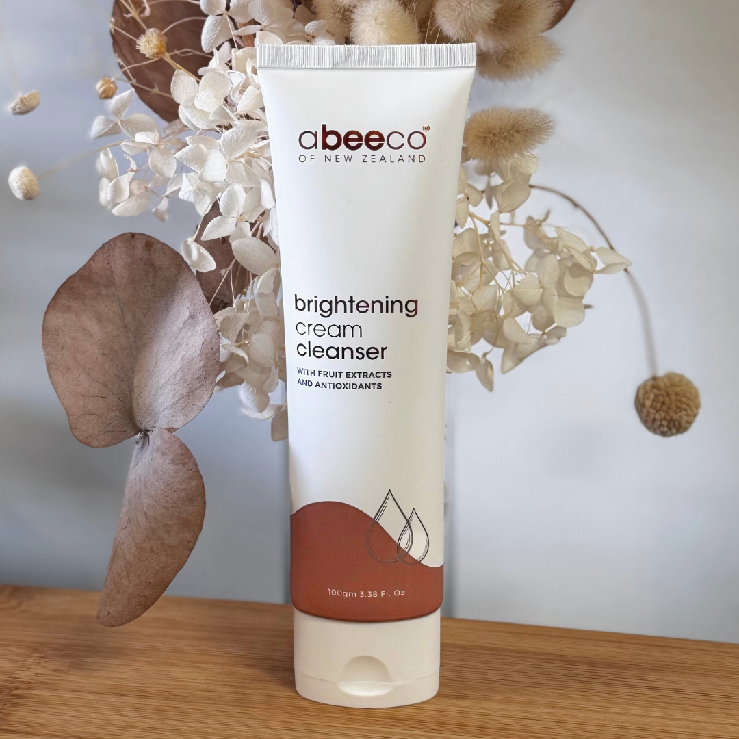Tube of abeecco brightening cream cleanser on a wooden surface with decorative flowers in the background