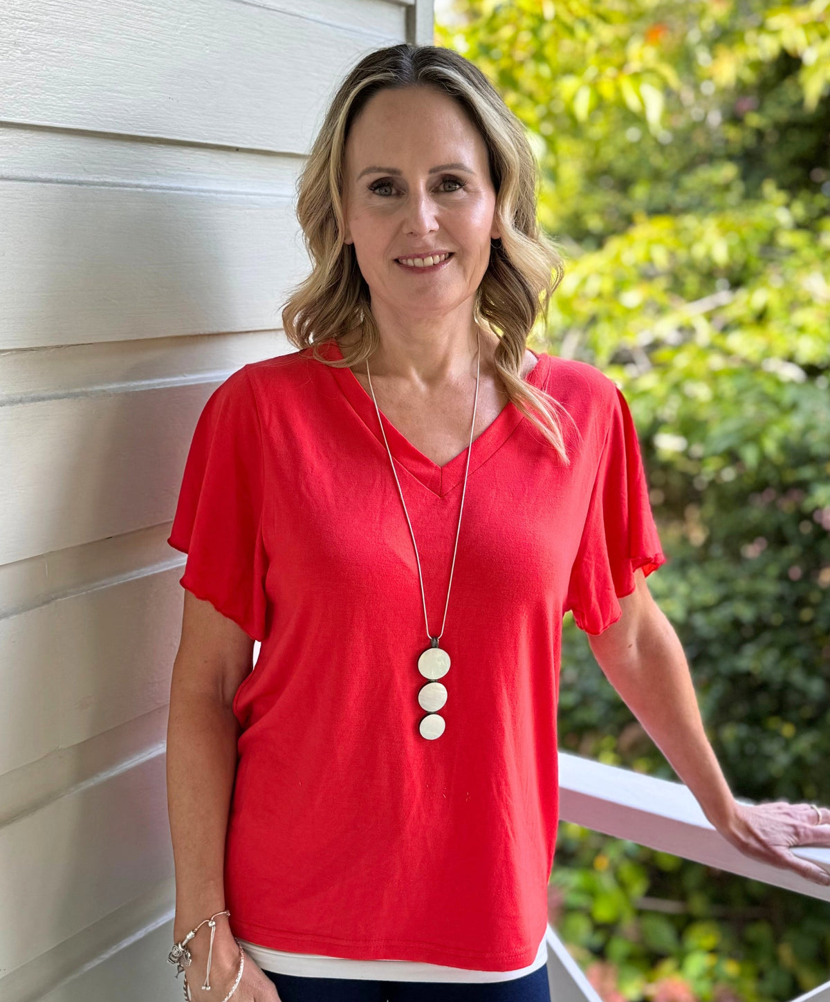Jude Salisbury in a red shirt standing on a balcony with greenery in the background