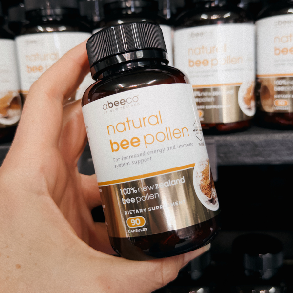 Hand holding a bottle of Abeeco natural bee pollen supplement with more bottles in the background.