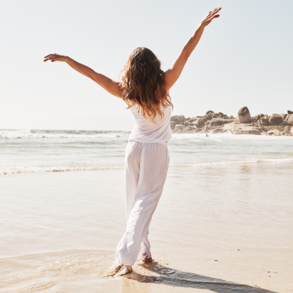 Woman in white outfit standing on a beach with arms outstretched