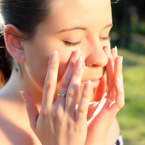 Woman with hands on face outdoors, sunlit